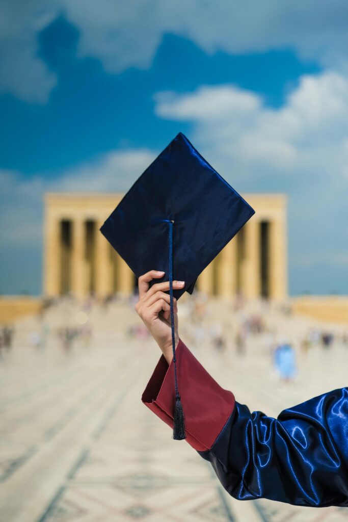 A graduate holding a cap in front of a blurred architectural background, symbolizing achievement.