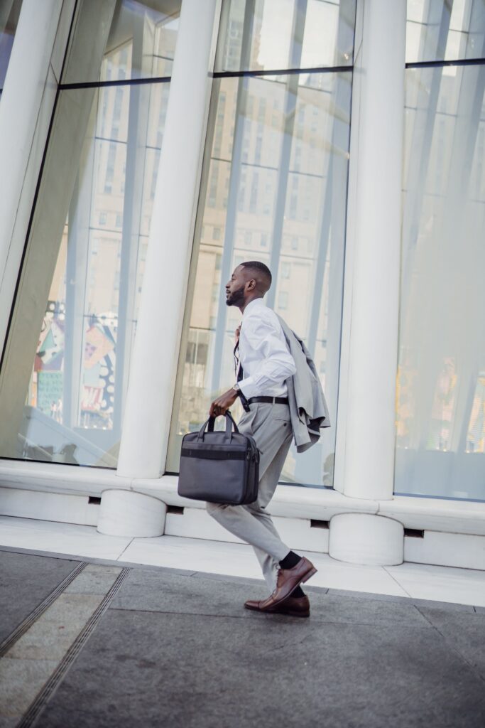 Elegant businessman in a suit, running outside a modern office building, carrying a briefcase.