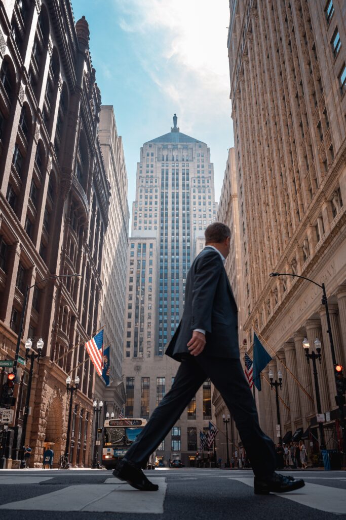 Businessman in suit crossing street in downtown Chicago with skyscrapers and flags.